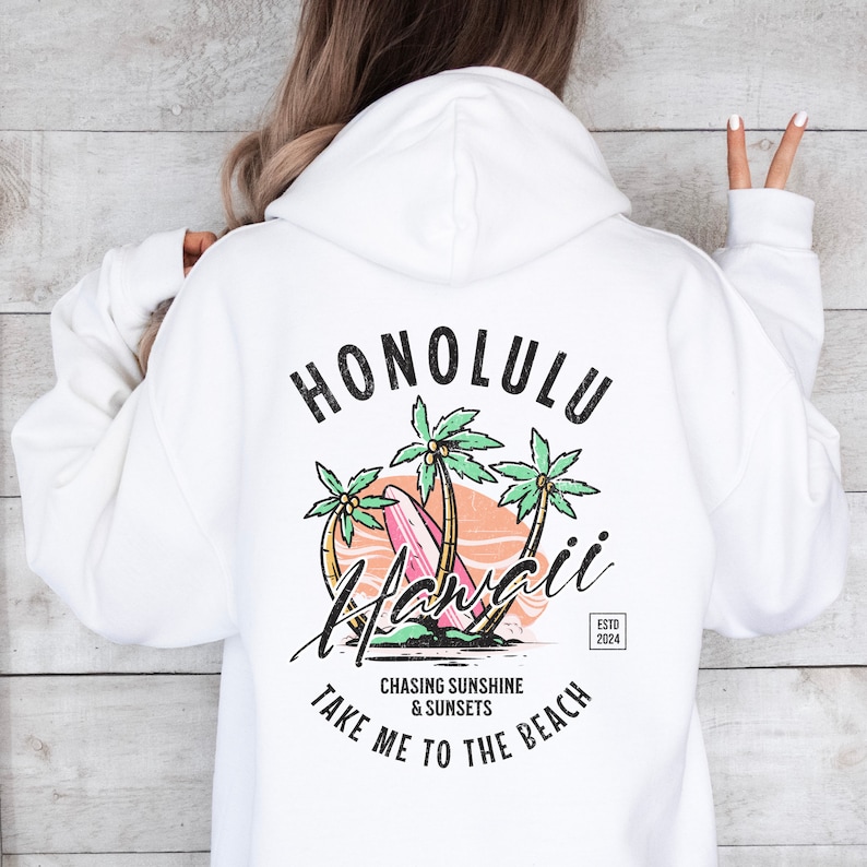 May include: White hoodie with a graphic print of palm trees, a surfboard, and the text "Honolulu Hawaii" in a vintage style. The text "Chasing Sunshine & Sunsets Take Me To The Beach" is printed below the graphic. The text "Estd 2024" is printed in a small font in the bottom right corner.
