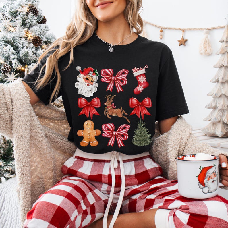 Pu&ograve; includere: T-shirt nero con grafica a tema natalizio. Il design include Babbo Natale, fiocchi rossi, una renna, un omino di pan di zenzero, una calza natalizia e un albero di Natale. La persona indossa un pigiama a quadri rossi e bianchi e tiene in mano una tazza con un disegno di Babbo Natale.
