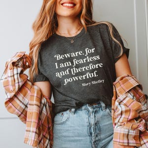 Puede incluir: Una camiseta gris oscura con el texto "Beware, for I am fearless and therefore powerful. - Mary Shelley" impreso en blanco.
