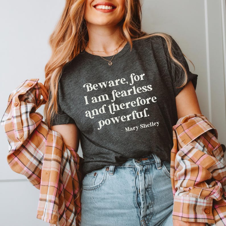 Puede incluir: Una camiseta gris oscura con el texto "Beware, for I am fearless and therefore powerful. - Mary Shelley" impreso en blanco.