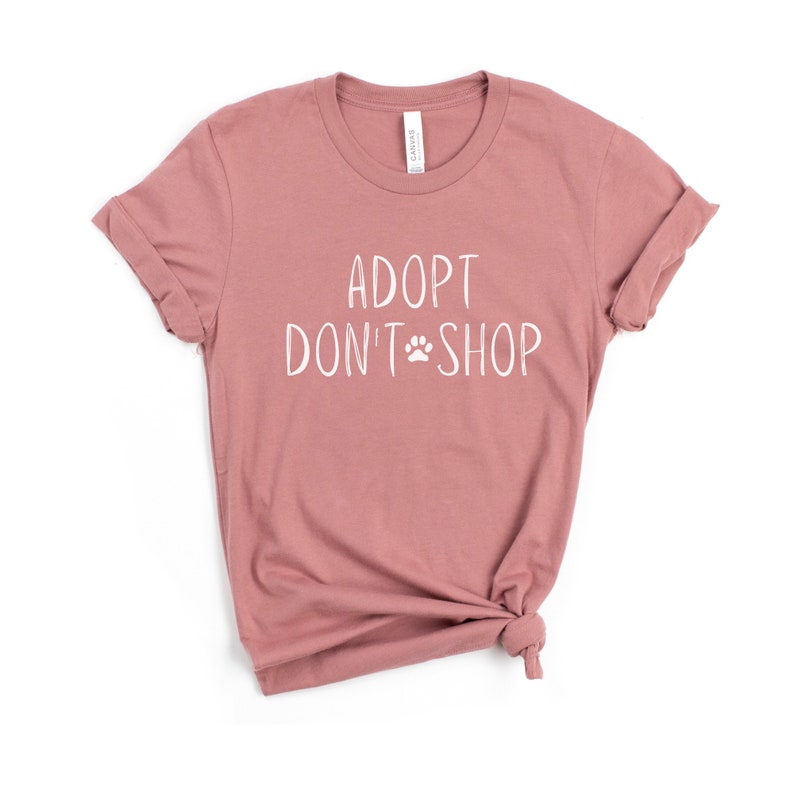 May include: A dusty rose t-shirt with the text "Adopt Don't Shop" in white with a paw print symbol.