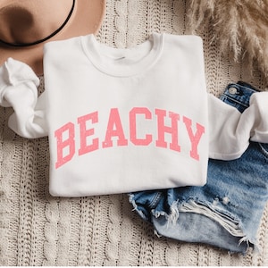 May include: White sweatshirt with the word "BEACHY" printed in pink letters.