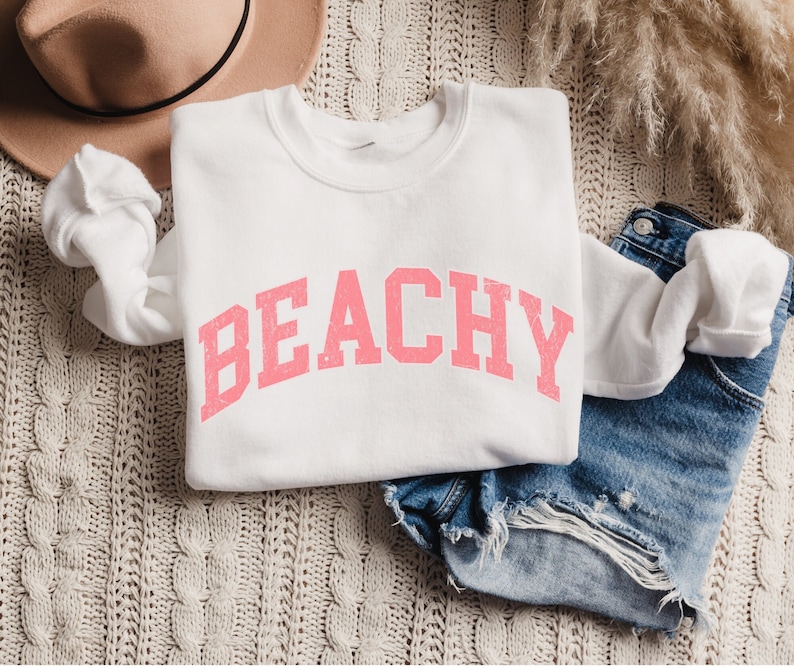May include: White sweatshirt with the word "BEACHY" printed in pink letters.