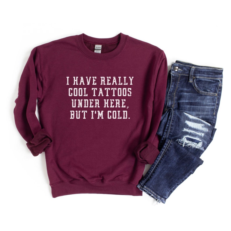 May include: Burgundy sweatshirt with the text "I have really cool tattoos under here, but I'm cold."