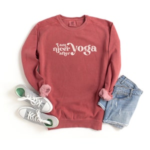 May include: A maroon sweatshirt with the text "I am nicer after yoga" in white. The sweatshirt is laid flat on a white surface with a pair of gray sneakers and a pair of blue denim shorts.