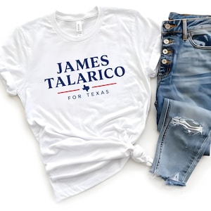 May include: A white short-sleeved t-shirt featuring the dark blue text JAMES TALARICO above a red horizontal line with a small blue Texas state silhouette and the text FOR TEXAS below, paired with blue denim jeans with distressed details.