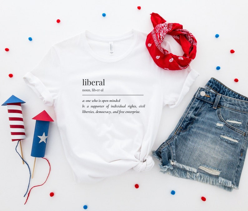 May include: White t-shirt with the definition of the word "liberal" printed on it. The definition is: "noun, lib-er-al a: one who is open-minded be a supporter of individual rights, civil liberties, democracy, and free enterprise."