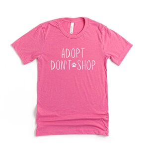 May include: Pink t-shirt with the text "Adopt Don't Shop" in white with a paw print between the words.