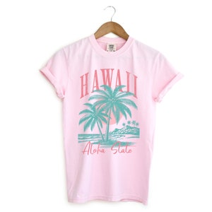 May include: Pink t-shirt with a graphic of palm trees and the text "Hawaii Aloha State" in a vintage style.