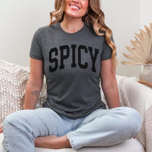 May include: A dark grey t-shirt with the word "SPICY" printed in black block letters.