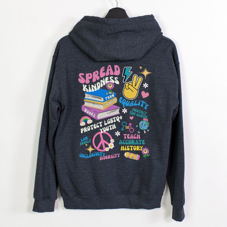 May include: A dark gray hooded sweatshirt with a colorful graphic print on the back. The graphic includes the words "Spread Kindness", "Equality", "Protect LGBTQ+ Youth", "Teach Accurate History", and "Live Freely".