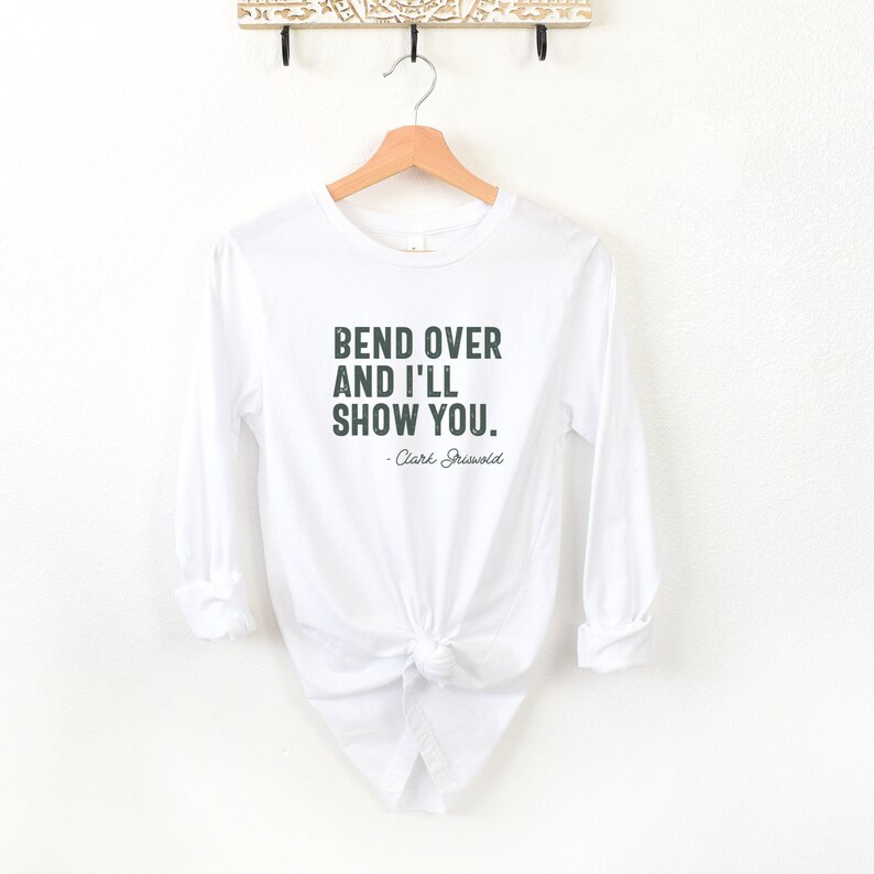 May include: White long-sleeved t-shirt with a green text graphic that reads "Bend over and I'll show you. - Clark Griswold".