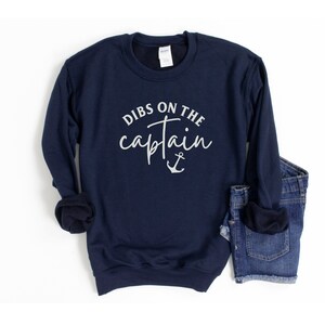 Puede incluir: Sudadera azul marino con el texto "Dibs on the captain" y un gr&aacute;fico de ancla en blanco.