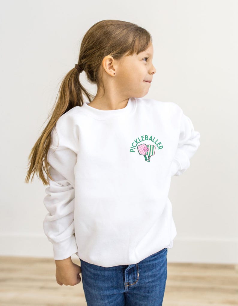 May include: White sweatshirt with a green and pink pickleball paddle graphic and the text "Pickleballer" on the front.