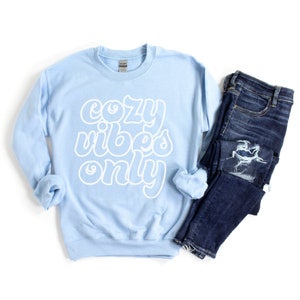 May include: A light blue sweatshirt with the text "cozy vibes only" in white outlined letters.