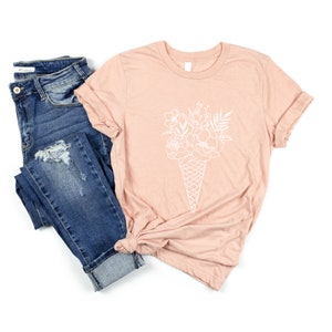 May include: A light pink t-shirt with a white outline of a bouquet of flowers in an ice cream cone.