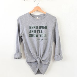 May include: Grey long-sleeved shirt with the text "Bend over and I'll show you." and "Clark Griswold" in a dark green font.