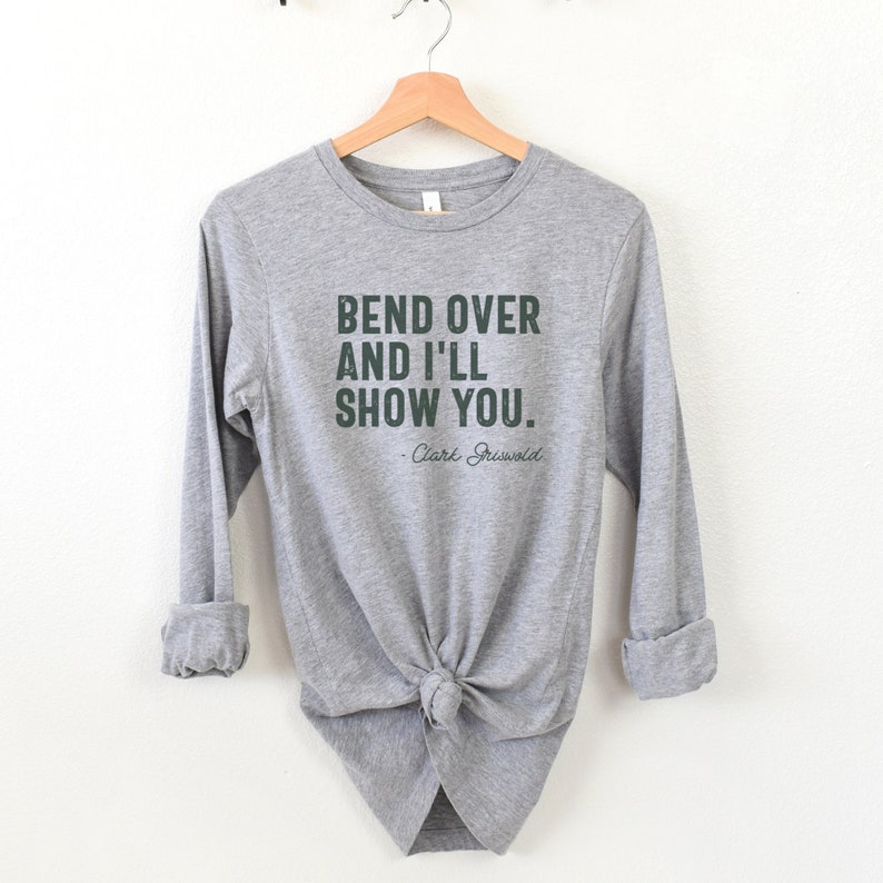 May include: Grey long-sleeved shirt with the text "Bend over and I'll show you." and "Clark Griswold" in a dark green font.