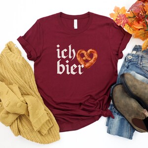 Op de afbeelding: Een maroon t-shirt met de tekst "ich &hearts; bier" in wit, met een hartvormige pretzel.