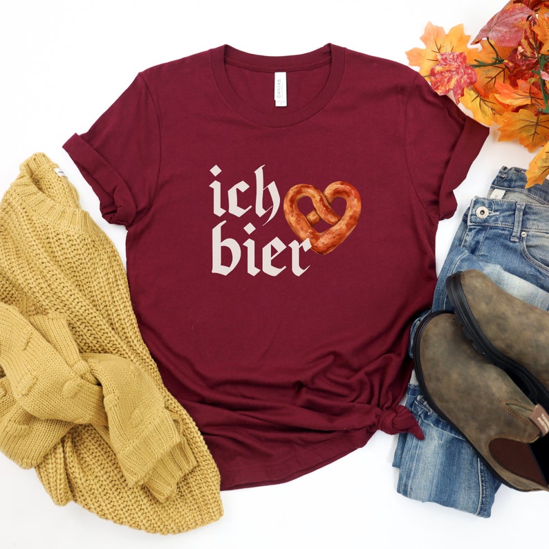 Op de afbeelding: Een maroon t-shirt met de tekst "ich &hearts; bier" in wit, met een hartvormige pretzel.