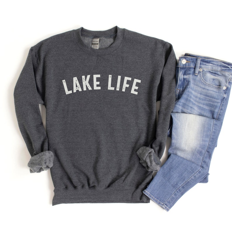 May include: A dark gray sweatshirt with the text "LAKE LIFE" printed in white on the front. The sweatshirt is shown with a pair of blue jeans.