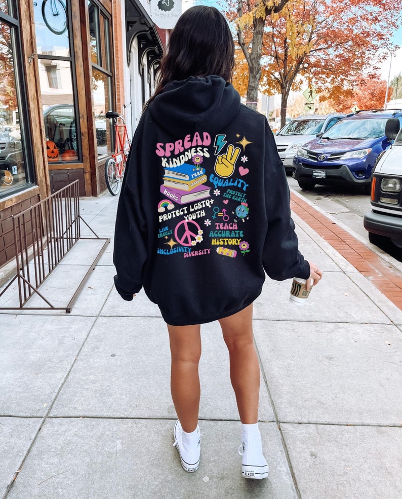 May include: Black hoodie with a colorful graphic print on the back. The graphic includes the words "Spread Kindness", "Equality", "Protect LGBTQ+ Youth", "Teach Accurate History", "Inclusivity", and "Diversity".