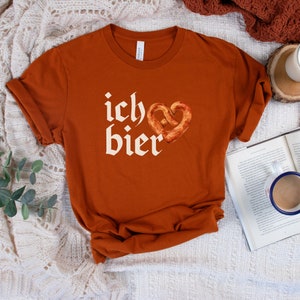 Op de afbeelding: Een roestkleurig T-shirt met de Duitse zin "ich &hearts; bier" in wit gedrukt. Het hart is een pretzel.