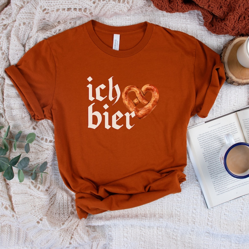 Op de afbeelding: Een roestkleurig T-shirt met de Duitse zin "ich &hearts; bier" in wit gedrukt. Het hart is een pretzel.