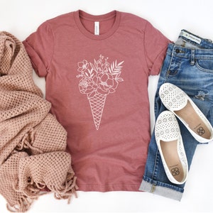May include: A mauve t-shirt with a white graphic of a bouquet of flowers in an ice cream cone.
