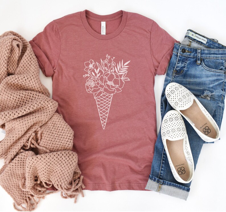 May include: A mauve t-shirt with a white graphic of a bouquet of flowers in an ice cream cone.