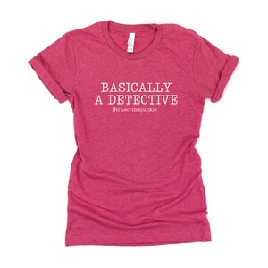 May include: A pink t-shirt with the text "BASICALLY A DETECTIVE #truecrimejunkie" in white.