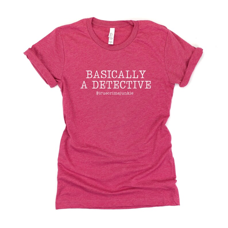 May include: A pink t-shirt with the text "BASICALLY A DETECTIVE #truecrimejunkie" in white.