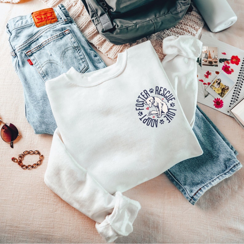 May include: White long-sleeve sweatshirt with a graphic of a dog and the text "Foster Adopt Love Rescue".