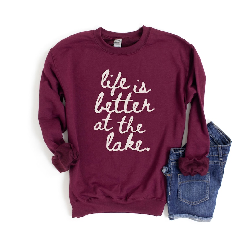 Op de afbeelding: Bordeauxkleurig sweatshirt met de tekst "life is better at the lake" in witte letters.