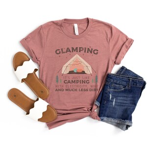 May include: A mauve t-shirt with the text "GLAMPING It's just like camping with electricity, wine and much less dirt" and a cartoon illustration of a tent with fairy lights.