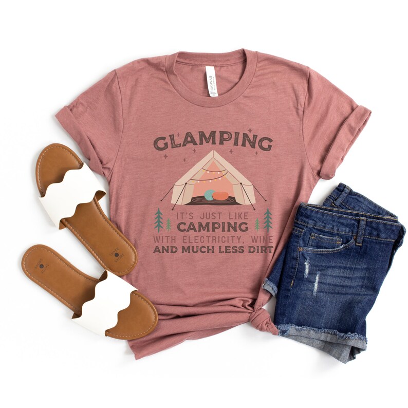 May include: A mauve t-shirt with the text "GLAMPING It's just like camping with electricity, wine and much less dirt" and a cartoon illustration of a tent with fairy lights.