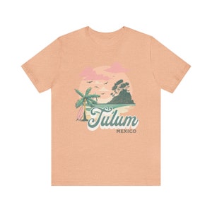 May include: A light peach t-shirt with a graphic of a palm tree, a surfboard, and a sunset over a small island. The text "Tulum Mexico" is printed below the graphic.