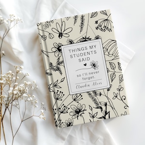 Peut inclure: Un journal crème avec un motif floral et le texte "THINGS MY STUDENTS SAID so I'll never forget." La couverture présente un dessin au trait noir de fleurs et de feuillage. Le nom de l'auteur, Claudia Alves, est également imprimé sur la couverture.