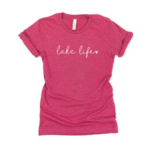 K&ouml;nnte beinhalten: Ein pinkfarbenes T-Shirt aus Heather-Material mit dem Text "lake life" in wei&szlig;er Kursivschrift und einem kleinen wei&szlig;en Herz.