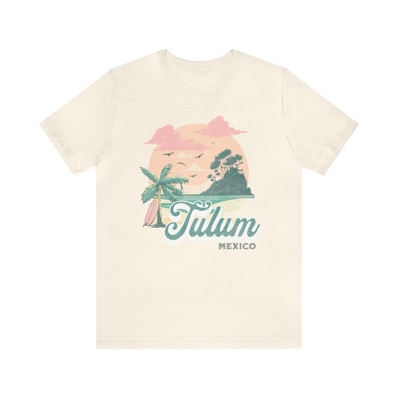 May include: A beige t-shirt with a graphic design of a palm tree, a surfboard, a small island, and a sunset. The text "Tulum Mexico" is printed below the graphic.