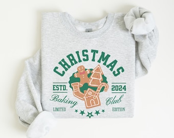 Könnte beinhalten: Ein graues Sweatshirt mit einem grünen und braunen Weihnachts-Backclub-Design. Das Design zeigt einen Lebkuchenmann, ein Lebkuchenhaus, einen Weihnachtsbaum und einen Zuckerstock. Der Text lautet "Christmas Baking Club Est. 2024 Limited Edition".