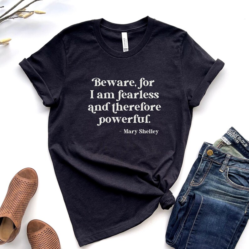 Puede incluir: Una camiseta gris oscuro con una cita blanca que dice "Beware, for I am fearless and therefore powerful. - Mary Shelley".