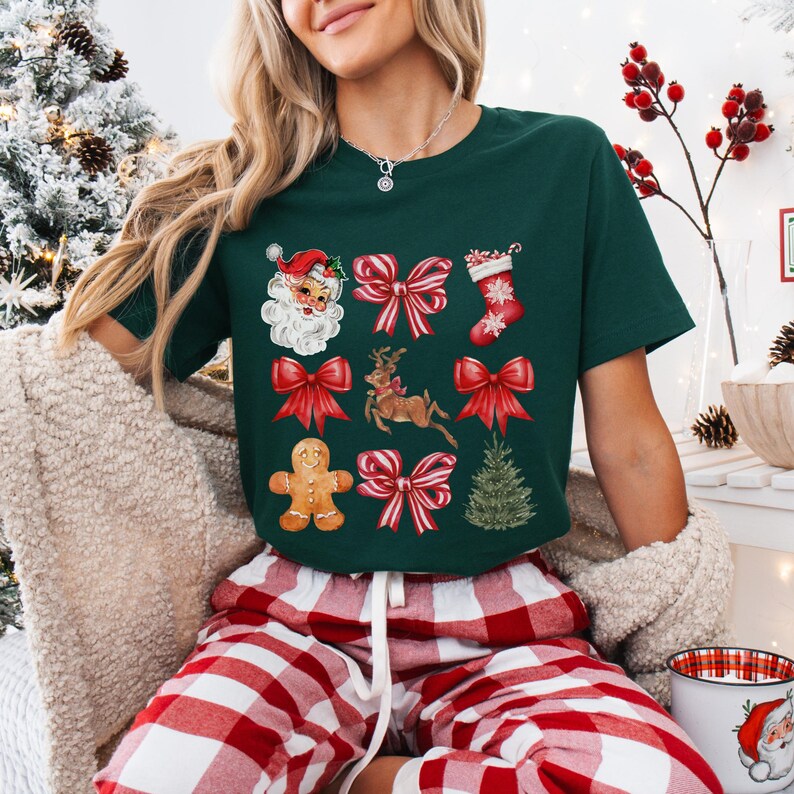 Pu&ograve; includere: Una maglietta verde scuro con illustrazioni a tema natalizio. Il design include Babbo Natale, fiocchi rossi, una renna, un omino di pan di zenzero, una calza natalizia e un albero di Natale. La persona indossa pantaloni da pigiama a quadri rossi e bianchi.