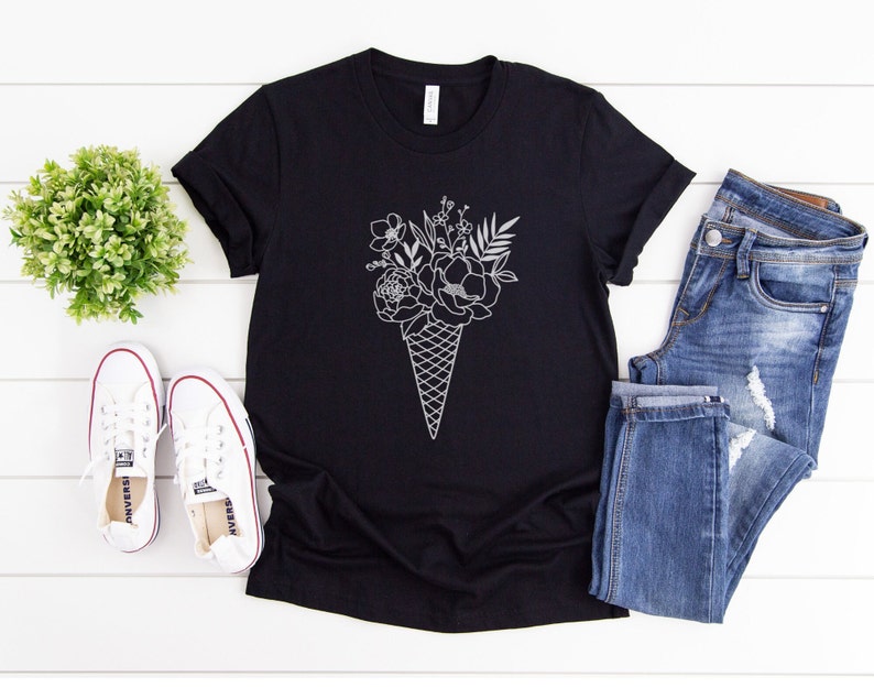 May include: Black t-shirt featuring a white outline of a bouquet of flowers in an ice cream cone.
