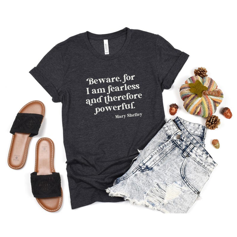 Puede incluir: Una camiseta gris oscuro con una cita blanca que dice "Beware, for I am fearless and therefore powerful. - Mary Shelley".