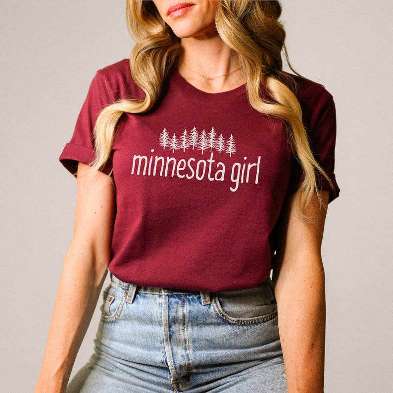 May include: A maroon t-shirt with a white graphic of pine trees and the text "minnesota girl".