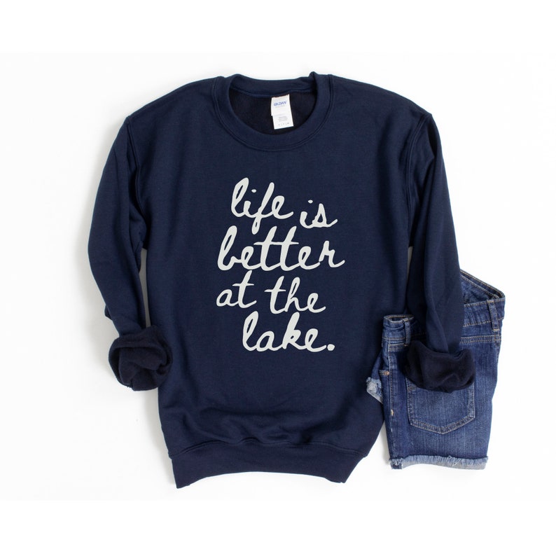 Op de afbeelding: Donkerblauwe trui met de tekst "life is better at the lake" in witte letters.