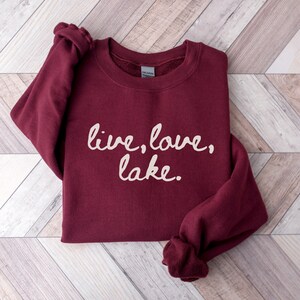 May include: Burgundy sweatshirt with the text "live, love, lake." in white.