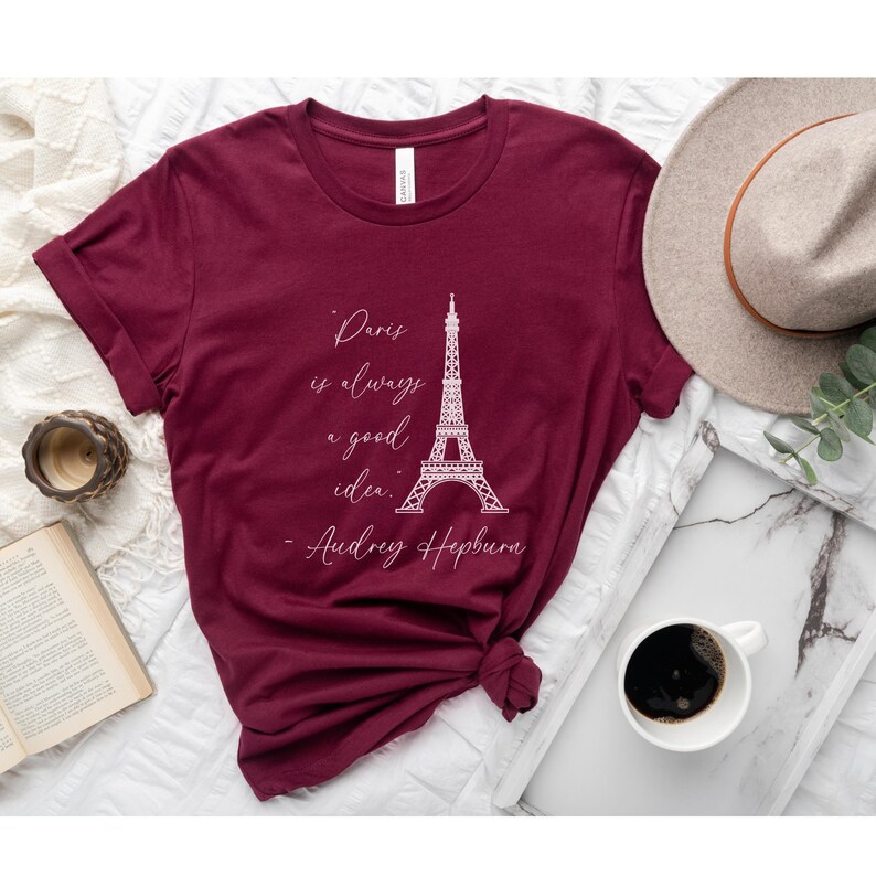 K&ouml;nnte beinhalten: Burgunderfarbenes T-Shirt mit einer wei&szlig;en Grafik des Eiffelturms und dem Zitat "Paris ist immer eine gute Idee. - Audrey Hepburn".