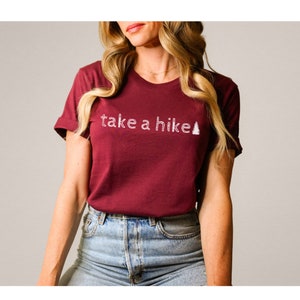 May include: A maroon t-shirt with the text "take a hike" and a white outline of a pine tree.